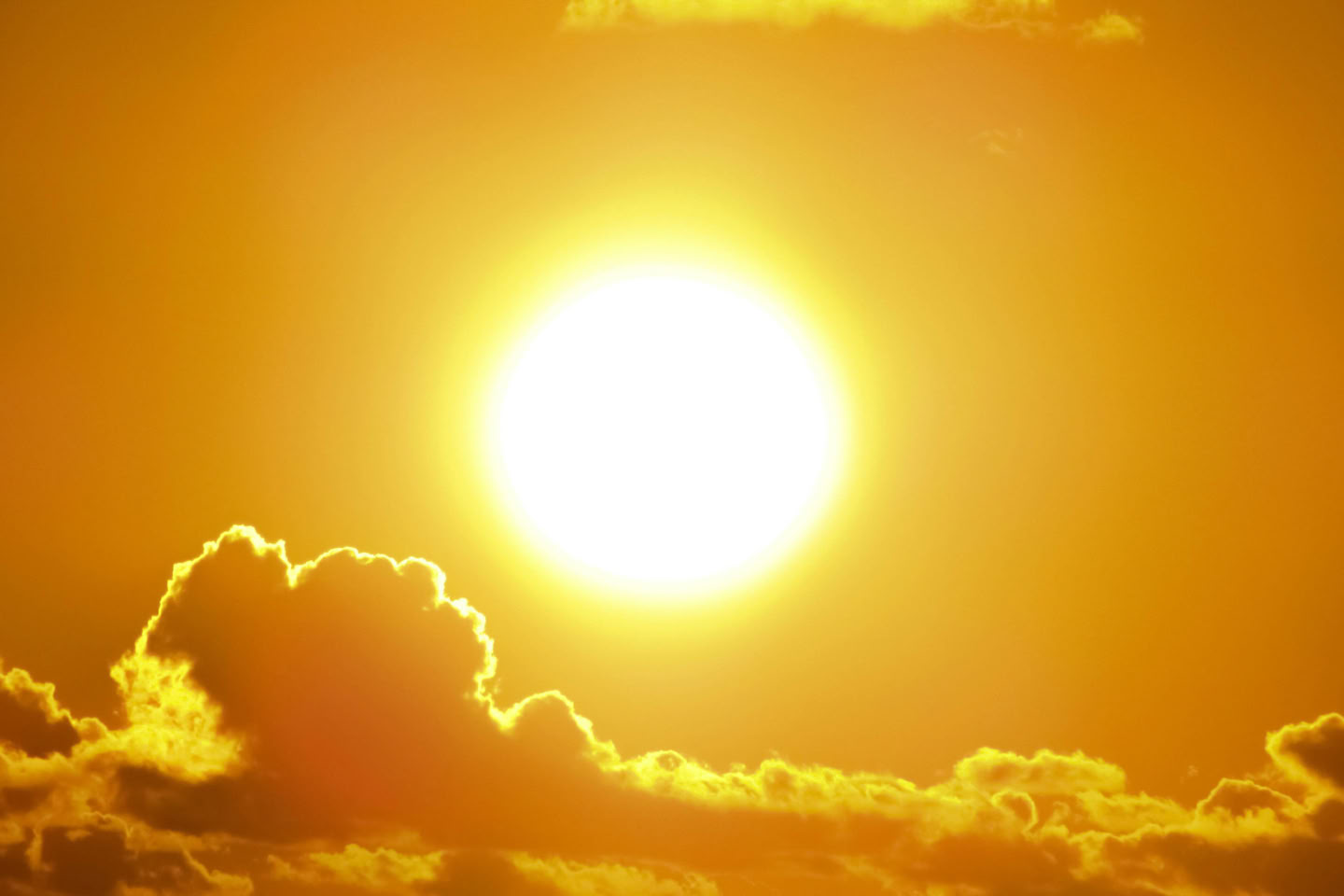 Bright sun in a clear sky with clouds at the bottom.