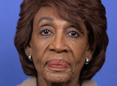 An older person with short brown hair, wearing a beige blazer and a silver necklace, against a blue background.